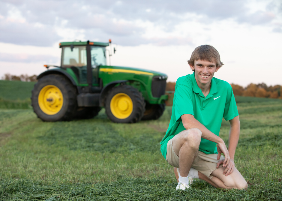 Owen Newland squats down in front of a John Deere tractor.
